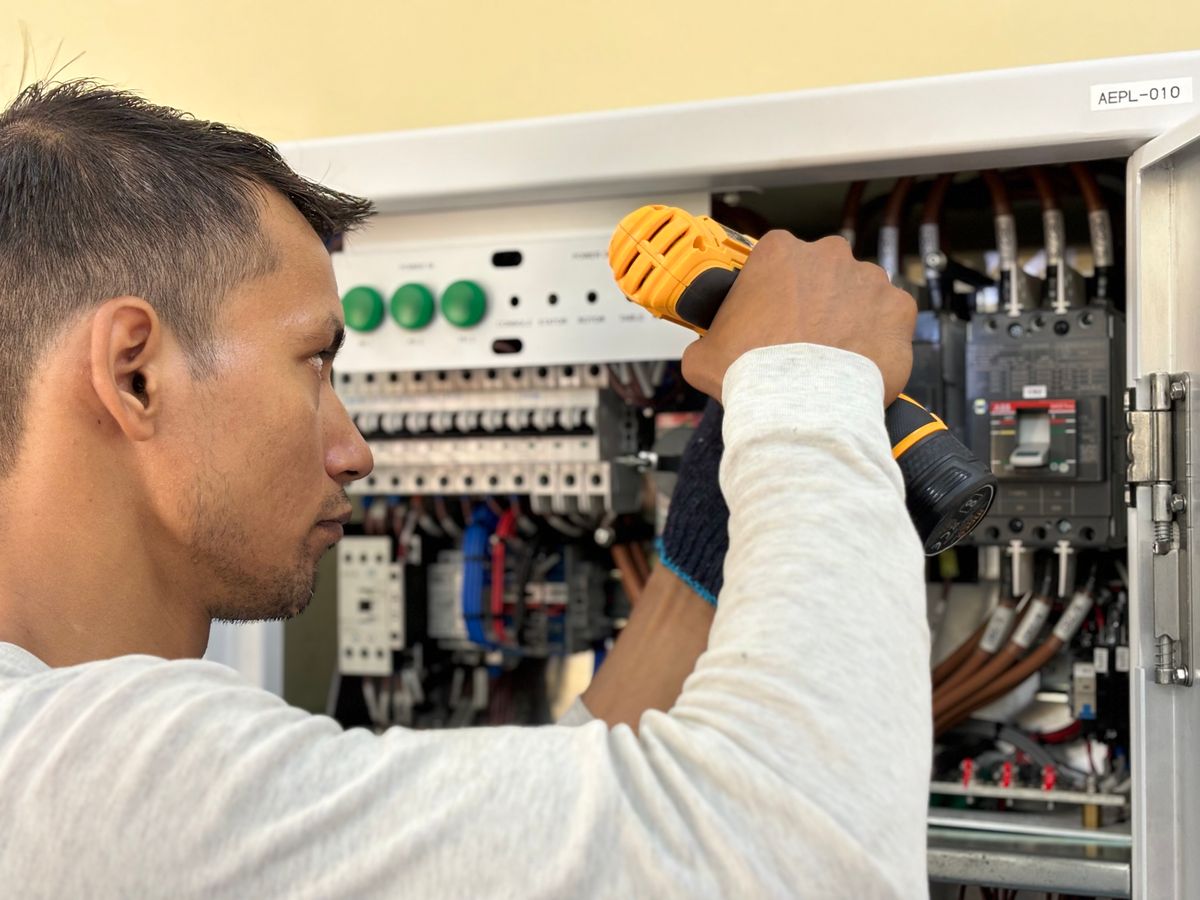 Technician using a drill inside an open electrical control panel